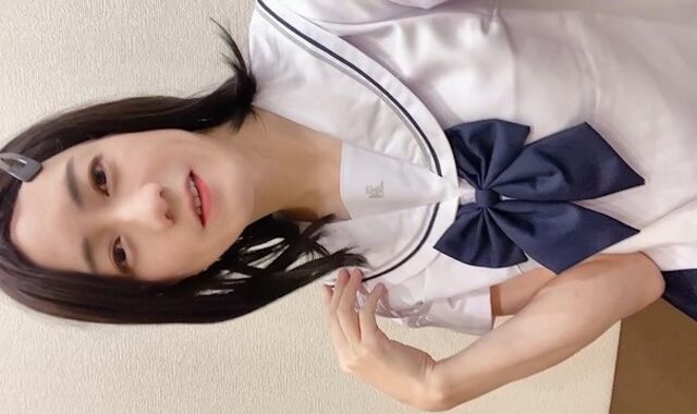 A crossdresser dressed in a Chinese high school uniform jerks with her M-shaped legs opened up